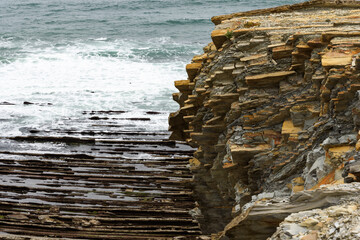 shoreline with rows of rocks in vertical strata on the seaside coast, with small waves on the French atlantic coast