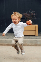 Playful little boy with blond hair jumping on the street with croissant in hand