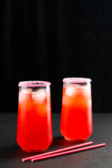 Refreshing summer mocktails with ice cubes. Two tall glasses of iced red juice with straws on dark background. Copy space, vertical orientation.