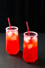 Refreshing summer mocktails with ice cubes. Two tall glasses of iced red juice with straws on dark background. Copy space, vertical orientation.