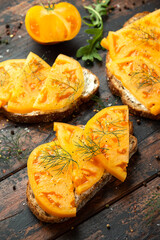 Vegetarian Sourdough toasts with soft cheese and orange beefsteak tomatoes on rustic wooden background