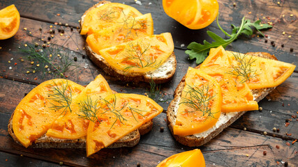 Vegetarian Sourdough toasts with soft cheese and orange beefsteak tomatoes on rustic wooden background