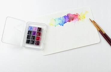 Empty Post card on white texture background with watercolor color paints and brushes. Flat lay. Top...