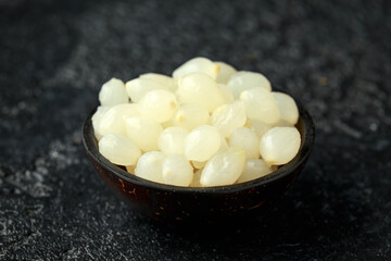 Pickled Cocktail Onions in wooden bowl on rustic black background