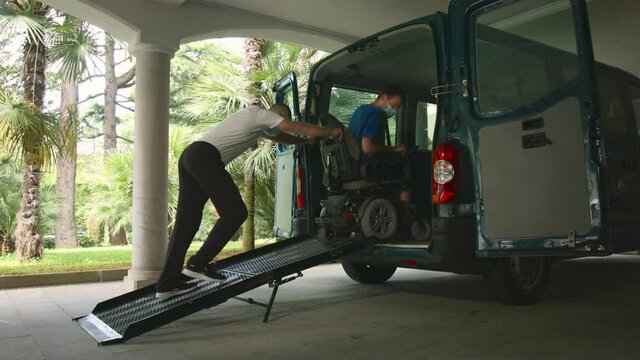 Man on wheelchair using accessible vehicle with ramp for transportation with driver helping.