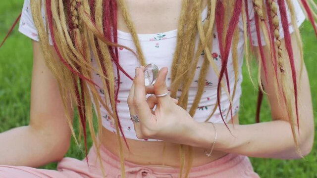 Outdoors portrait of a girl with dreadlocks hairstyle holding in hand little natural stone rock crystal, rhinestone