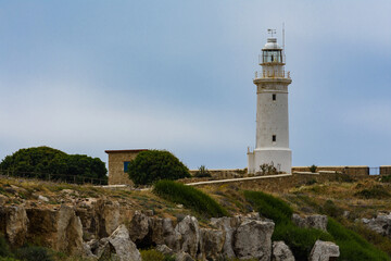 Fototapeta na wymiar Beautiful cyprus lighthouse at the background of cloudy autumn sky. Grey rocks are in the foreground