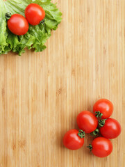 Ripe cherry tomatoes with green lettuce on a wooden background