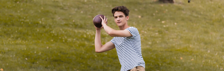Fototapeta premium panoramic crop of teenager boy playing american football in park