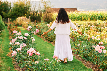 Obraz na płótnie Canvas Woman enjoying nice day in beautiful rose garden, wearing white clothes