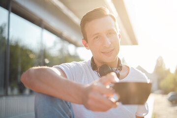 Young attractive man enjoying a cup of aromatic coffee outdoors in sunny weather