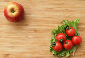 Ripe cherry tomatoes with green lettuce on a wooden background