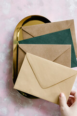 Brown paper, green and beige envelopes on golden tray and pink background. 