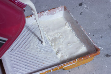 The plasterer pours the primer from the canister. Worker pours the primer into the paint tray