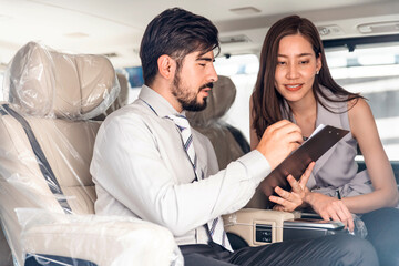 Car Dealership. The Asian Salesman (woman) checking the list with the middle east customer inside the new car with plastic wrapped seats before hand over. Automotive Leasing and Dealing Business.