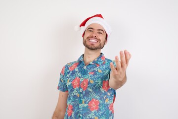 Young caucasian man wearing hawaiian shirt and Santa hat over isolated white background smiling friendly offering handshake as greeting and welcoming. Successful business.