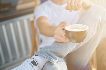 Young attractive man enjoying a cup of aromatic coffee outdoors in sunny weather