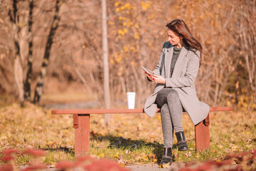 Fall concept - beautiful woman drinking coffee in autumn park under fall foliage