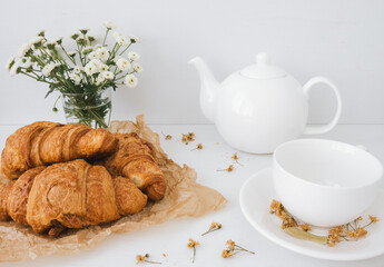 Closeup of delicious croissant in composition with white teapot and cup.