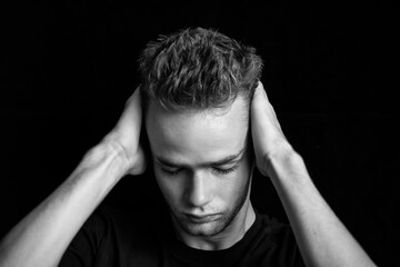 dramatic black and white portrait of sad embarrassed pensive teenager / young guy. Young man, unshaven, with a beard holding his head, black and white photo