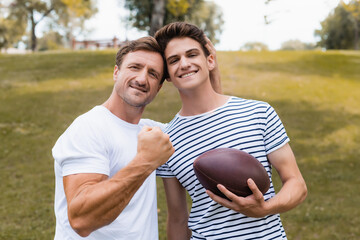 proud father showing clenched fist and standing near teenager son with rugby ball