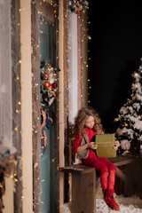 a little girl holds a box with a gift in her hands and sits on a bench on a snowy street