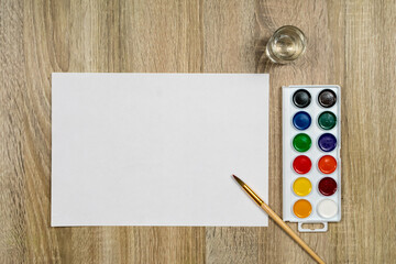 Watercolor paints and a brush with water on a wooden background. View from above. Place for an...