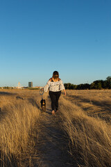 Attractive young woman with a white shirt and wearing a face mouth mask with her dog walking in the countryside. Masks are mandatory outside home during coronavirus COVID-19 outbreak in some countries