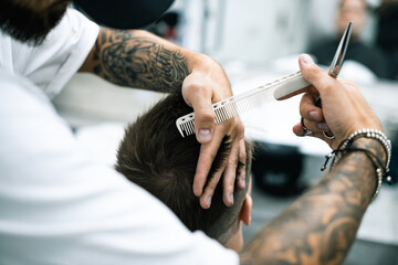 Selective focus of tattooed barber cutting hair of young man in barbershop 