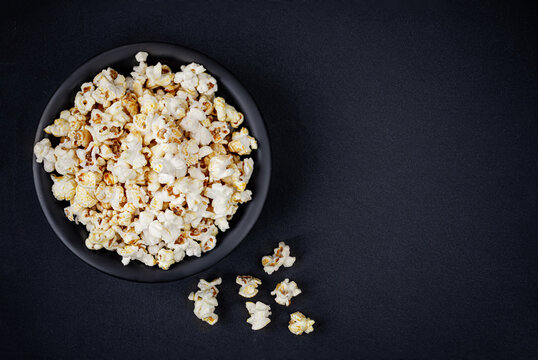 Scattered salted popcorn in a bowl  on black background with copy space. Homemade Popcorn  Top view. .