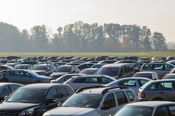 Parked cars on a green field. In the background is a forest.