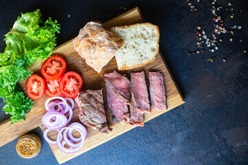 sandwich meat and vegetables loaf of bread, tomato, lettuce, medium or rare steak on the table serving size top view copy space for text food background rustic