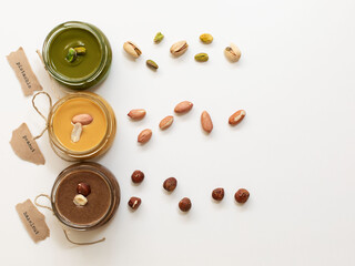 Nuts butter in jars with ingredients. Homemade raw organic peanut, hazelnut, pistachio, nuts paste butter. Top view. Copy space.