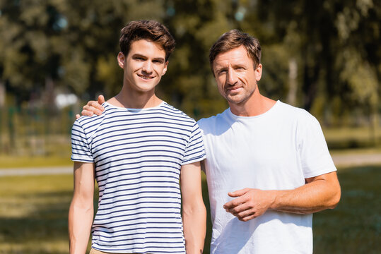 father standing and hugging teenager son in park