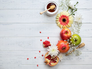 Rosh Hashanah Jewish New Year holiday concept. 
Creative layout of traditional symbols - apples, honey, pomegranate isolated on white wooden background, top view, copy space.