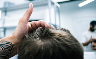 Cropped view of barber applying hair volumizer on client hair during hairstyle in barbershop 