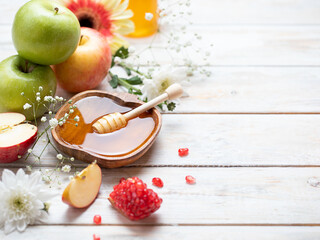 Rosh Hashanah Jewish New Year holiday concept with traditional symbols - apples, honey, pomegranate on white wooden background. Copy space.