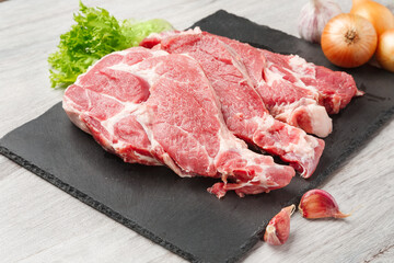Several sliced steaks of pork neck with ingredient on black stone board on gray kitchen table. Close up view.