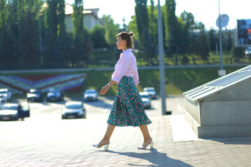 A young beautiful brunette girl with a strong square walks in a pink shirt and a green skirt. She enjoys, enjoys life