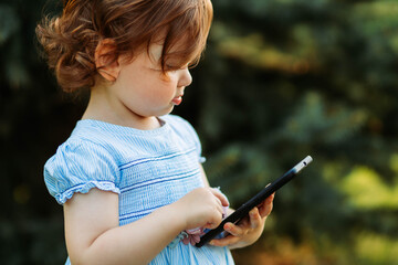 Cute, little two year old girl looks at the phone. Copy space