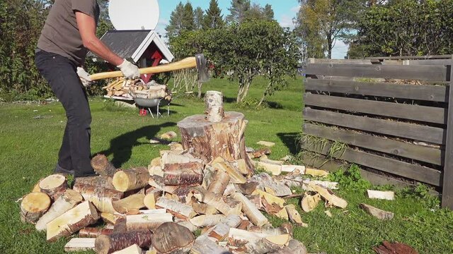 Mature Man Chopping birch log with large metal axe with yellow wooden handle, log splitting. He does not succeed from first time and try few times before log is chopped. Backyard, sunny, slow motion