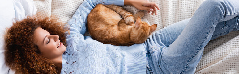 Horizontal crop of woman lying near cat on bed