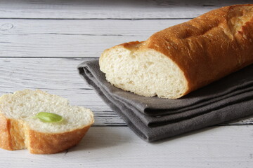 French fresh soft bread baguette on napkin and wooden background. Several cut pieces are lying next to each other.