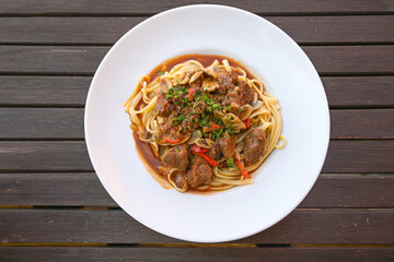 Beef ragout with red bell peppers and mushrooms with parsley garnish on pasta in a white plate on a rustic dark wooden table, high angle view from above, copy space