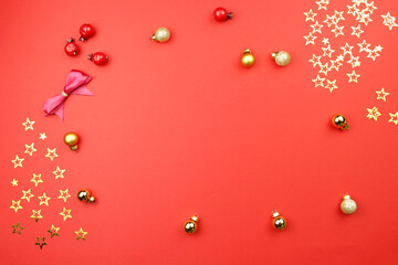 Fototapeta premium christmas decoration on red background with golden confetti stars, balls, berries. Concept holiday atmosphere, new year, celebration, greeting card. Flatlay, top view, frame, copyspace