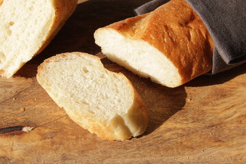 French fresh soft bread baguette on a wooden cutting Board. Several cut pieces are lying next to each other.