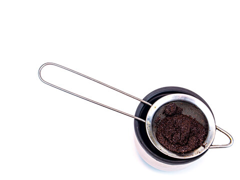 A strainer for filtering coffee or tea is poured into a cup. Metal strainer. Coffee and hot drinks. Preparing hot drinks. Filter. Kitchen dishes. Home kitchen. Tool. White background. Place for text.