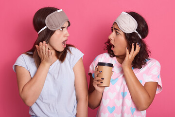 Two astonished dark haired females with widely opened mouths, girls hear shocking news, wearing...