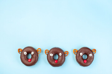 Three Christmas reindeers made from chocolate doughnut, pretzel cookie, marshmallow and candy, Christmas background with copy space, horizontal, top view