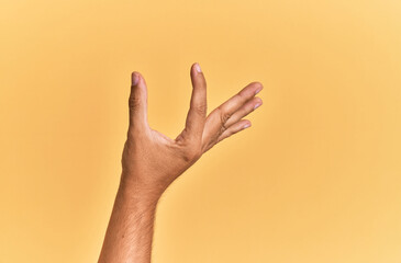Arm and hand of caucasian man over yellow isolated background picking and taking invisible thing, holding object with fingers showing space